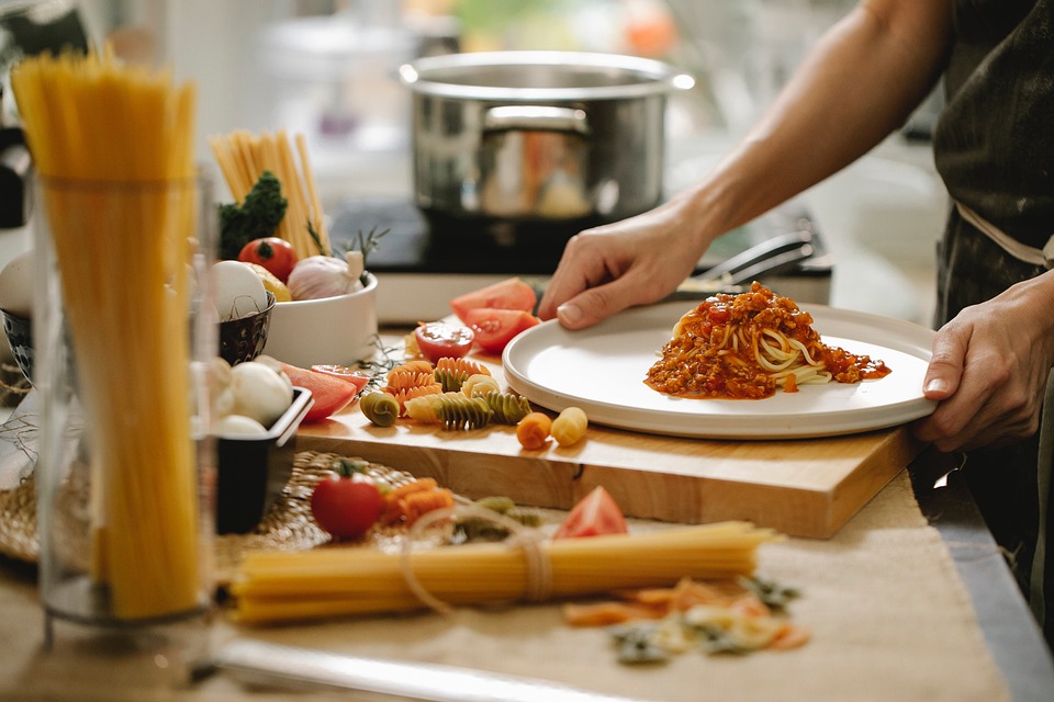 Bild på okokt spagetti liggande framför en skärbräda med grönsaker och kokta pasta  och en kastrull i bakgrunden